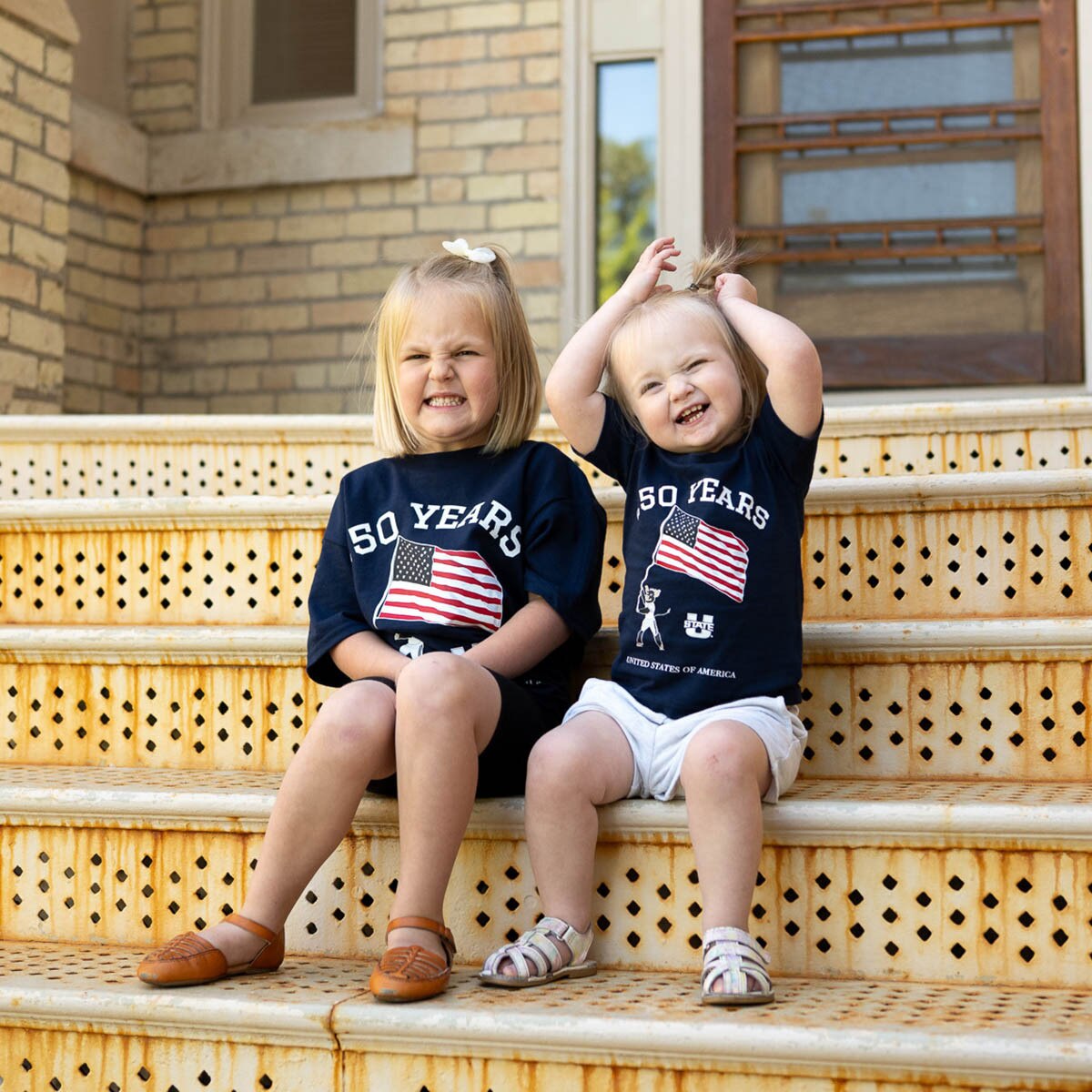 Two kids wearing matching patriotic tees on Old Main stairs